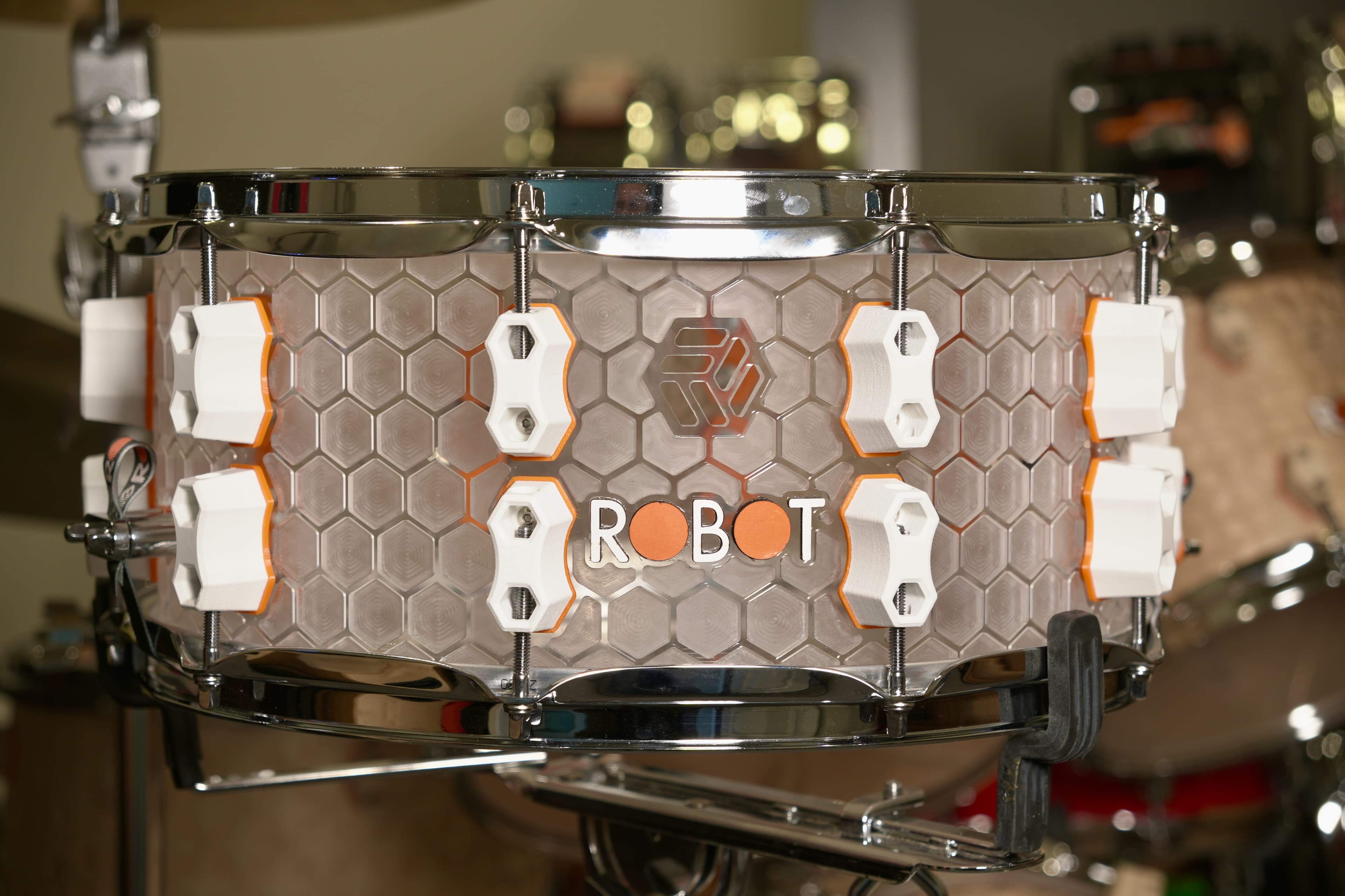 Close view of a clear Robot drum shell with printed white and orange hardware.